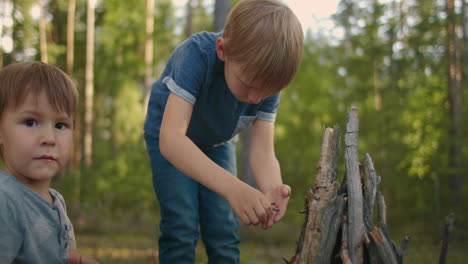 Two-boys-put-sticks-in-a-fire-in-the-woods-during-a-hike.-Boys-in-the-woods-prepare-to-light-a-fire-and-put-sticks-together