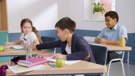 Male-Student-Sitting-At-Desk-In-English-Classroom-Writting-In-Her-Notebook-2