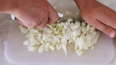 primer plano de la mano de un hombre cortando las cebollas en una pizarra blanca con un cuchillo de acero