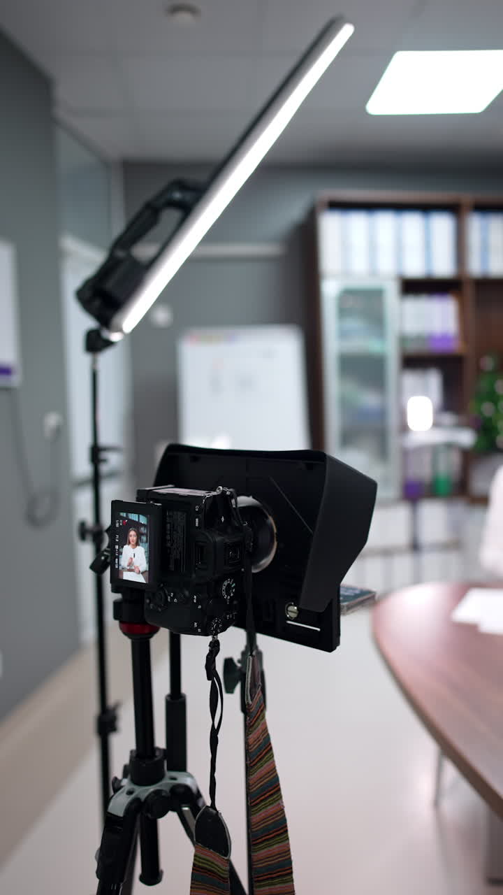 Approaching a camera filming a female speaker. Woman in white jacket recording her blog. Blurred backdrop. Vertical video.