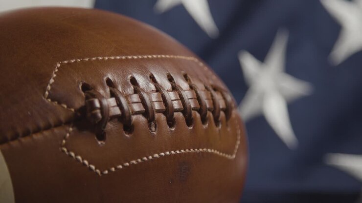 El enfoque se desplaza de un primer plano de una bandera de estrellas y barras a un balón de fútbol americano