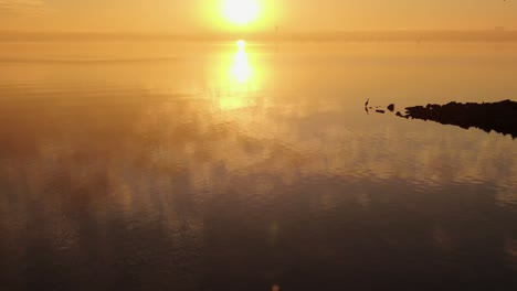 golden hour light spreads across haze on calm lake reflecting an orange glow onto water