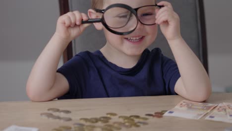 bebé caucásico con gafas jugando con euros, monedas, billetes y lupa