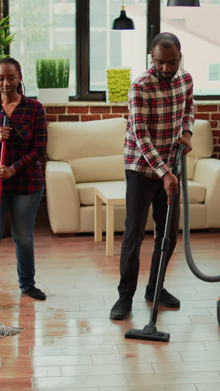 Vertical video: Young happy couple listening to music and washing floors in apartment