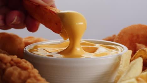 hand dipping a potato wedge into cheese sauce with other fast food items