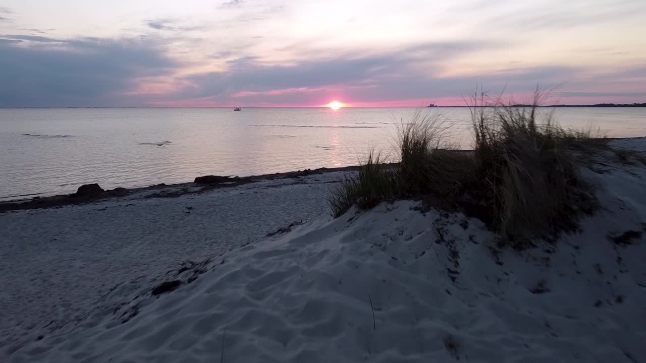 Solnedgang på en strand i Malmø, drone flyver lavt og afslører solnedgangen i baggrunden over bakken.