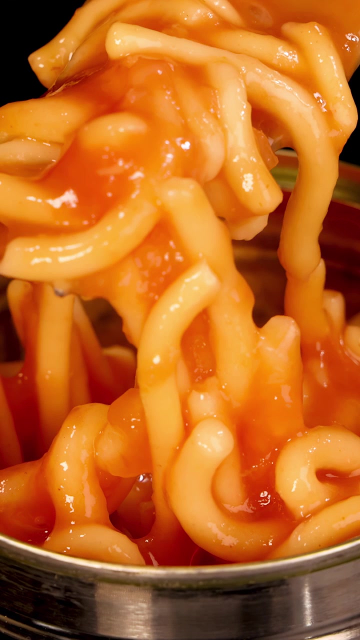 Una forchetta di metallo solleva spaghetti al sugo da una lattina aperta sotto un'illuminazione brillante e diretta, con una prospettiva ravvicinata e un movimento fluido della telecamera verso l'alto.