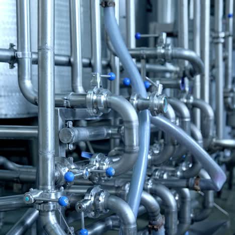 numerous pipes crossing with each other at modern milk factory enterprise. pipelines with valves and faucets. close up with gradual distancing