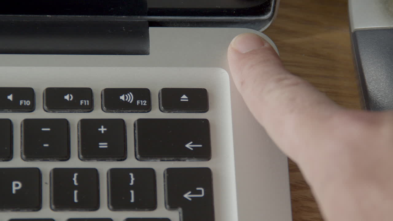 палец многократно нажимает на кнопку включения ноутбука - вид сверху вниз