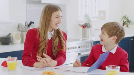 Portrait-Of-Laughing-Brother-And-Sister-Wearing-School-Uniform-Doing-Homework-On-Kitchen-Counter