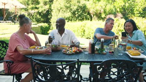 senior diverse friends enjoying in garden lunch, sharing stories and laughter at garden table