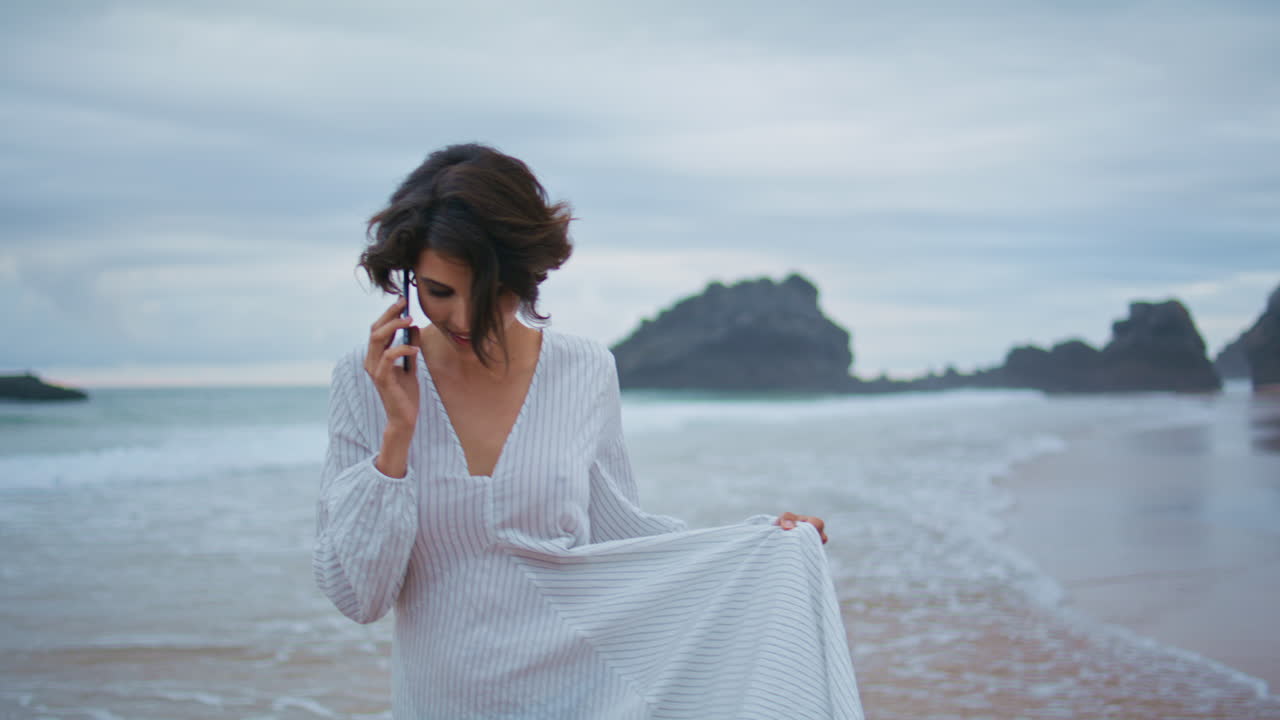 chica al aire libre hablando móvil en la playa rocosa. primer plano de mujer sonriente mirando cámara