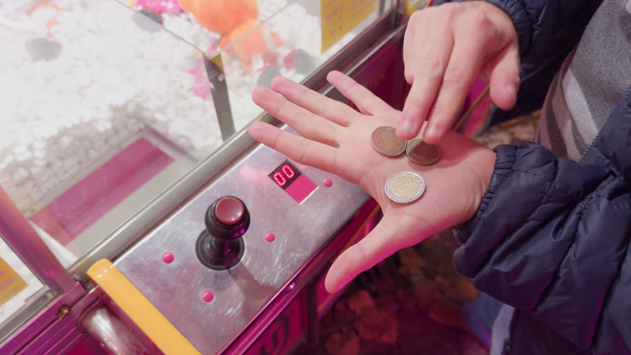 Hand holding coins by claw machine at night in Montrichard Val de Cher fair, France
