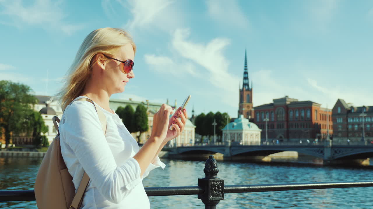 한 젊은 여성이 스웨덴 스톡홀름 시내를 배경으로 스마트폰을 사용합니다.