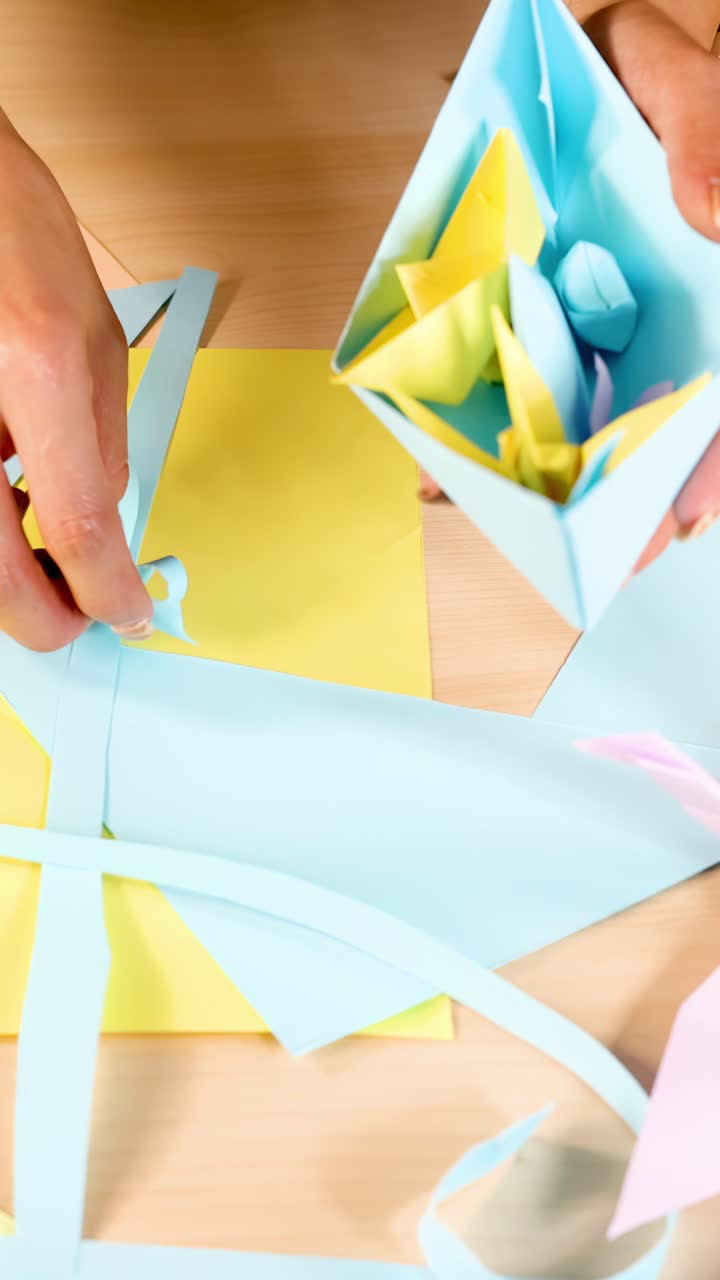 Una persona crea fiori di origami colorati usando carta pastello, vista dall'alto, illuminazione brillante e uniforme, telecamera stabile.