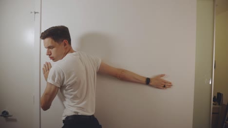 Un-Hombre-Con-Una-Camisa-Blanca-Estirando-Los-Brazos-Frente-A-La-Pared-Blanca