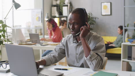 Black-Man-in-Headset-Working-Laptop-and-Speaking-on-Web-Call