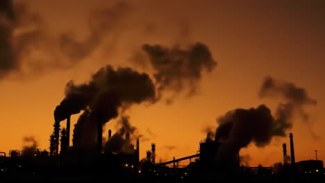 dramatic silhouette of industrial facilities against a fiery sunset, highlighting environmental impact with rising smoke and pollution levels