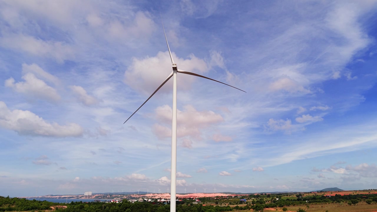 Le turbine eoliche si ergono alte a Hoa Thang, Lam Dong. Le nuvole si muovono lentamente nel cielo azzurro. L'area è luminosa e mostra il paesaggio. È una giornata limpida perfetta per ammirare il panorama