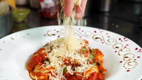 Chef-decorating-ravioli-with-tomatoes-sauce-in-restaurant-adding-parmesan-cheese,-close-up,-Mediterranean