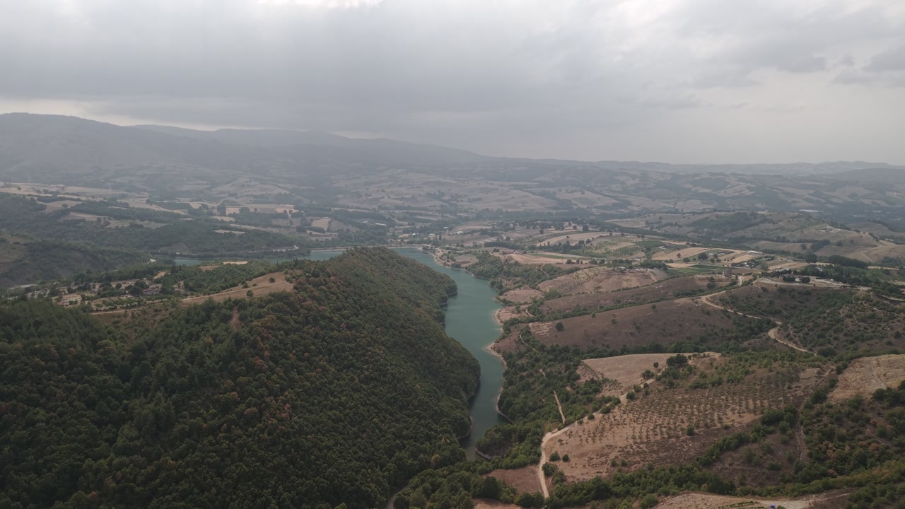 Aerial drone forward shot over the Yalakdere River flowing through green countryside and farmland in Gölcük, Kocaeli, Turkey on a cloudy day.
