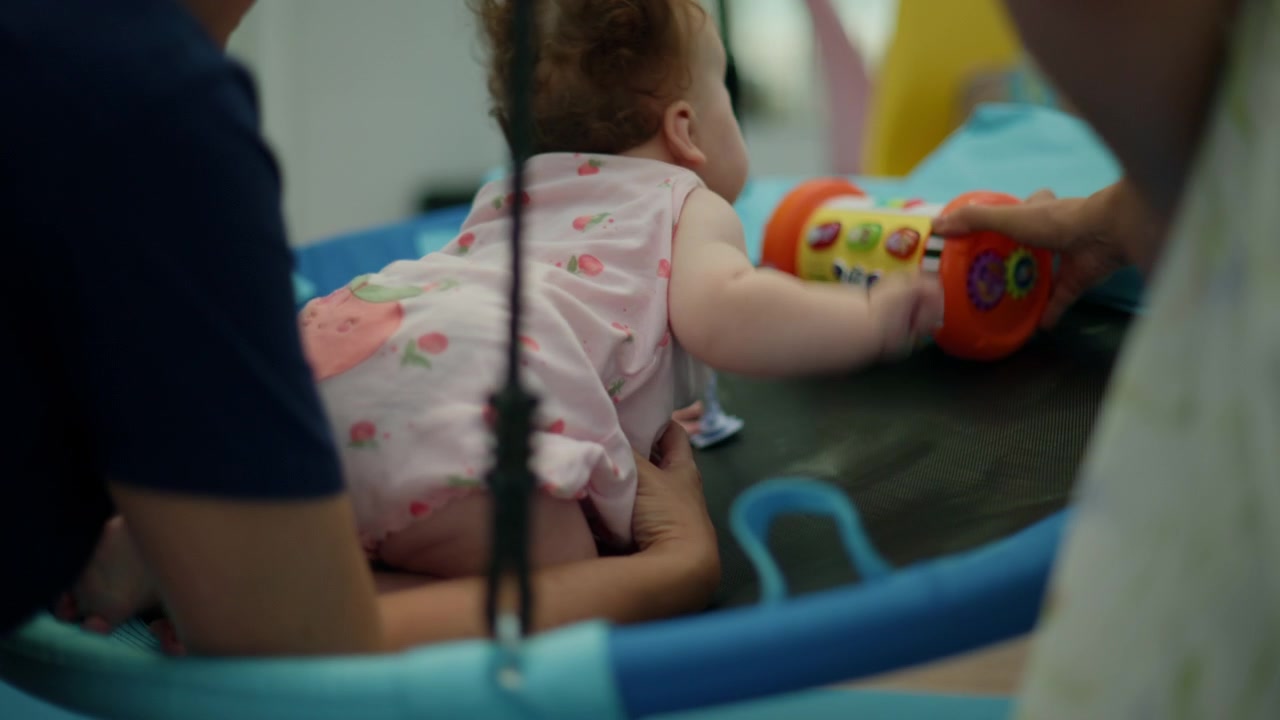 Bebê com cabelo cacheado aprendendo a engatinhar durante sessão de terapia de desenvolvimento, apoiado por um terapeuta que promove habilidades motoras