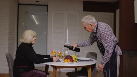 Senior-retired-couple-having-fun-drinking-wine-and-eating-meal-during-romantic-supper-in-kitchen