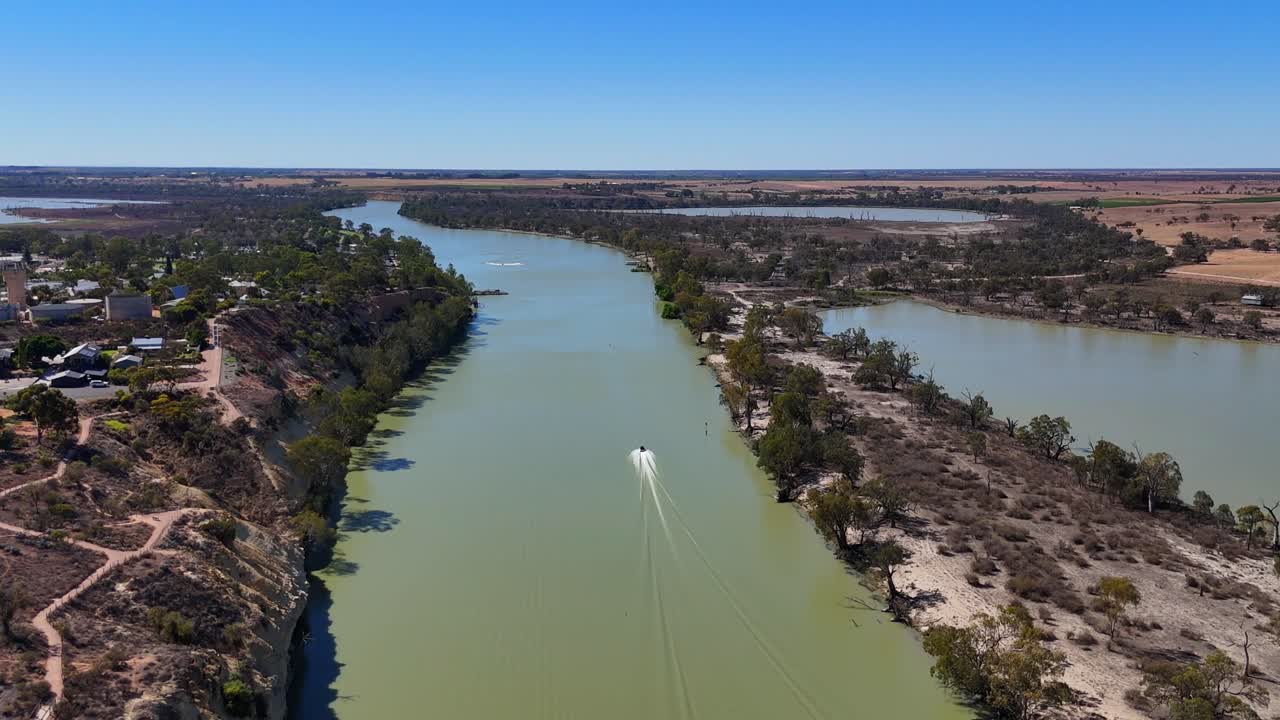 Der Waikerie-Flusskanal schlängelt sich vorbei an bebauten Ufern und offenem Land unter klarem Himmel, die Luftaufnahme verfolgt ein sich schnell bewegendes Boot