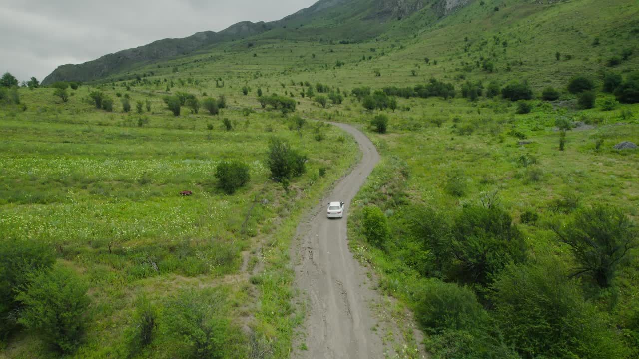 White Car Driving on a Dirt Road in a Green Mountain Valley