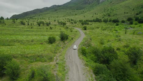 white car driving on a dirt road in a green mountain valley