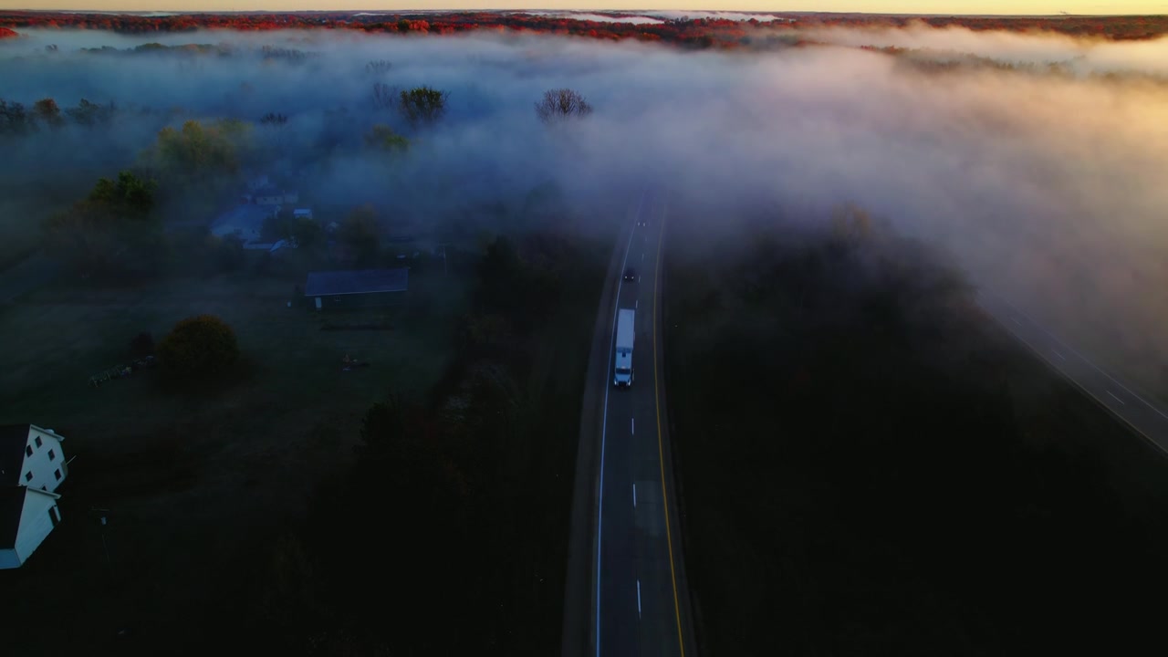 Rimorchio frigorifero bianco che viaggia su un'autostrada nebbiosa del Michigan con alberi autunnali e l'alba sullo sfondo