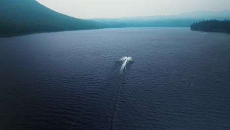 aerial rear view follows speed boat wake across open deep blue mountainous lake