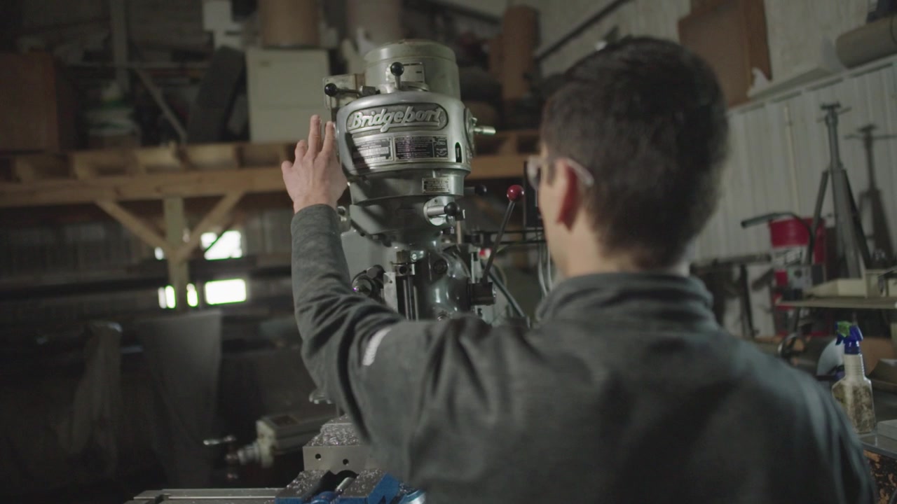 Una toma en cámara lenta desde el hombro (OTS) de un joven mecánico arrancando una vieja máquina Bridgeport en su taller