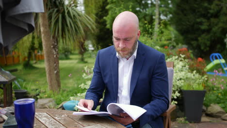 a man reading papers of a report sitting in his garden whilst working from home