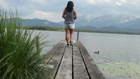 Frau,-Die-Einen-Holzsteg-Am-Hopfensee-Bei-Füssen-Hinuntergeht-Und-Die-Landschaft-Genießt,-Bayern,-Deutschland