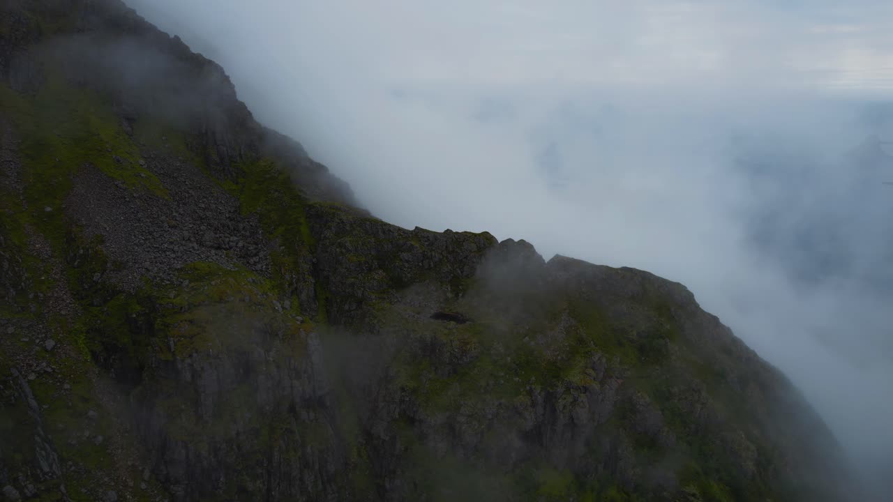 Aerial of green mountain range at scenic Lofoten Islands, Norway with blue sea. Flying through clouds.