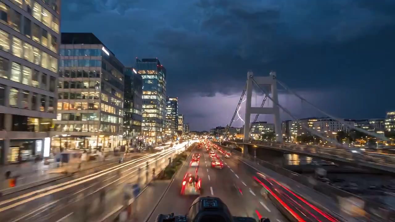 A bustling urban street scene at dusk showcasing vibrant market stalls, cityscape structures, and illuminated traffic against a twilight sky and heavy clouds.