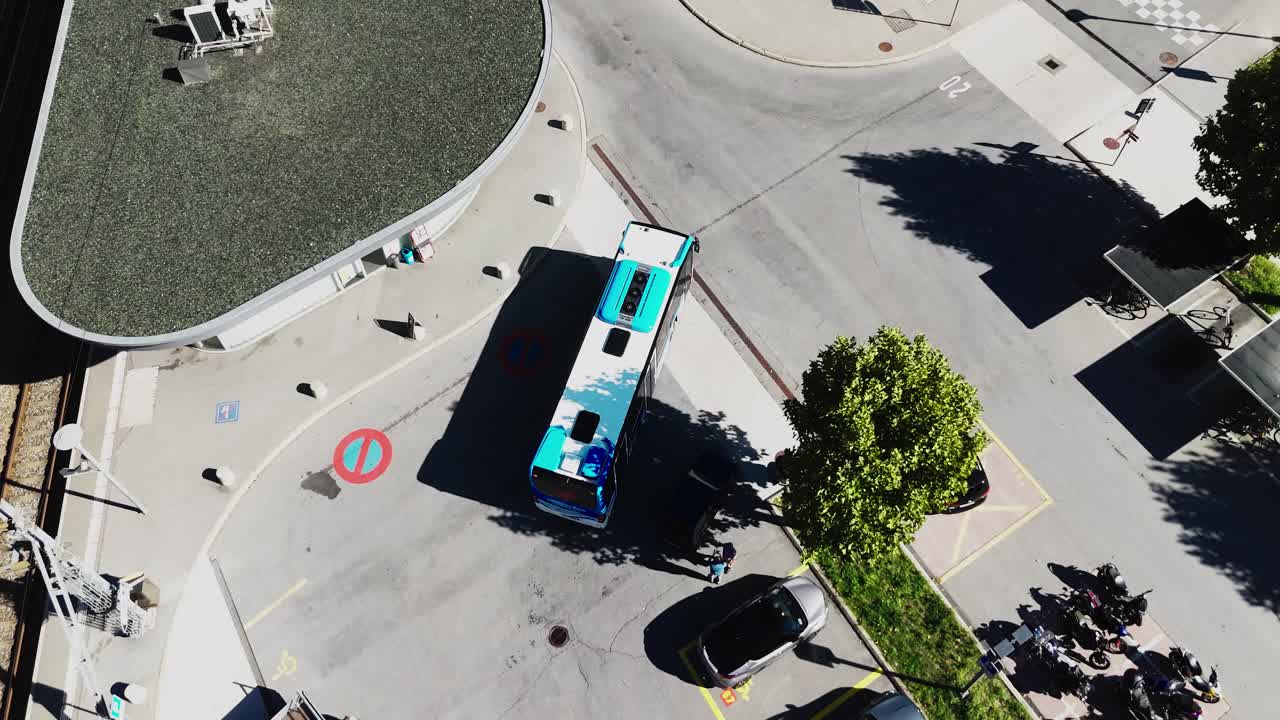 Drone footage of a blue and white city bus driving along an urban street intersection with trees and buildings. Concept for public transport, mobility, and city infrastructure