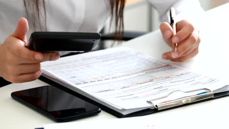 manos de la mujer contando en la calculadora y llenando documentos en la oficina moderna