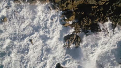 Top-View-Of-Foamy-Waves-Breaking-On-The-Rugged-Shoreline