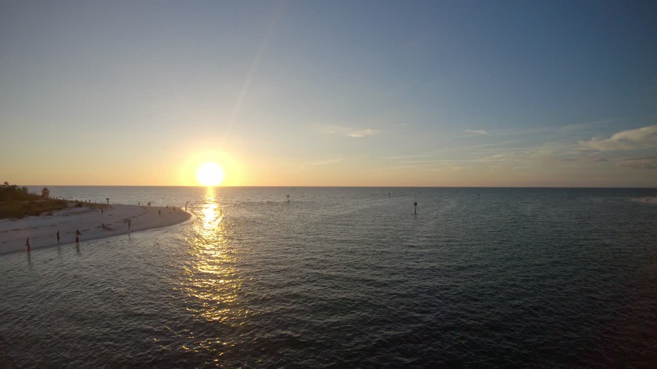 Drone video moving backwards into Wiggins Pass, Naples, Florida as the sun sets over the ocean. The beach either side of the pass.
