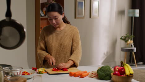 부에서 건강한 신선한 채소를 채식주의자 또는 채식주의자의 식사로 준비하는 여성, 보드 1에 빨간색과 노란색 고추를 잘라내는 여성.