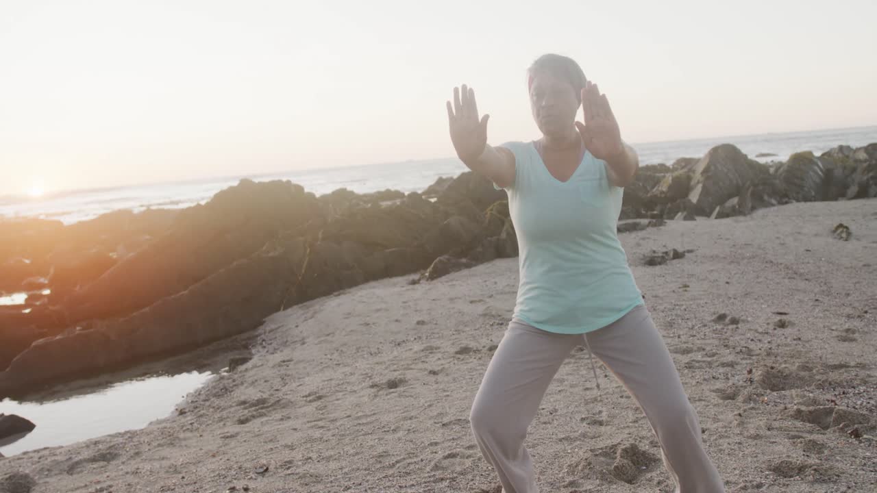 Donna afroamericana anziana che fa yoga e stretching in spiaggia, al rallentatore.