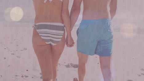 animation of lens flares and rear view of caucasian couple holding hands and walking at beach
