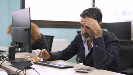 stressed businessman using computer at desk and sitting with head in hands in office