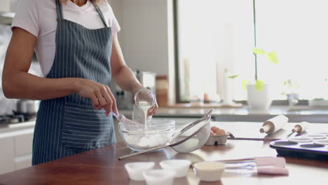 Midsection-of-biracial-woman-in-apron-mixing-cake-mix,-baking-in-kitchen,-copy-space,-slow-motion