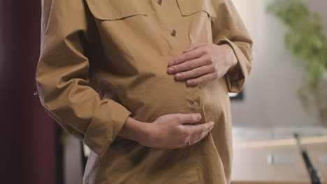 Close-Up-View-Of-Pregnant-Woman-Posing-At-Camera-While-Touching-Her-Belly-In-The-Office