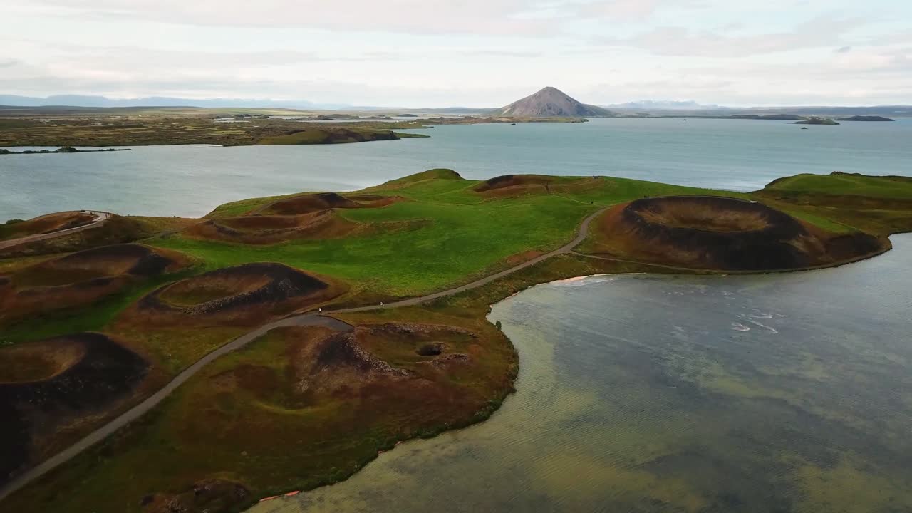 Aerial view capturing Skútustaðagígar pseudocraters reflecting beautifully in Lake Mývatn, surrounded by breathtaking Icelandic landscape in autumn hues of green, brown, and blue, establishing shot