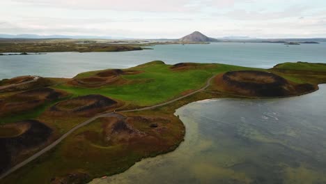 aerial view capturing skútustaðagígar pseudocraters reflecting beautifully in lake mývatn, surrounded by breathtaking icelandic landscape in autumn hues of green, brown, and blue, establishing shot