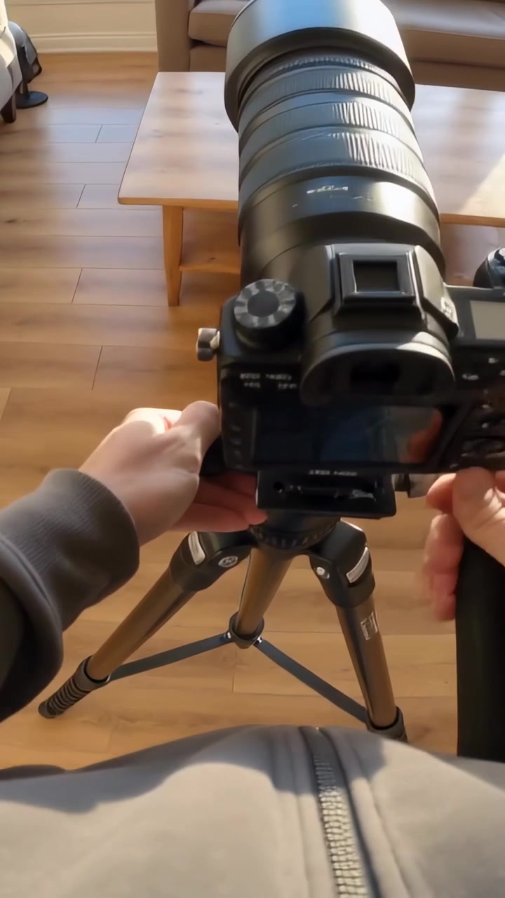 Vertical video: Carrying tripod adult in grey hoodie mounting tele camera at home aiming at window